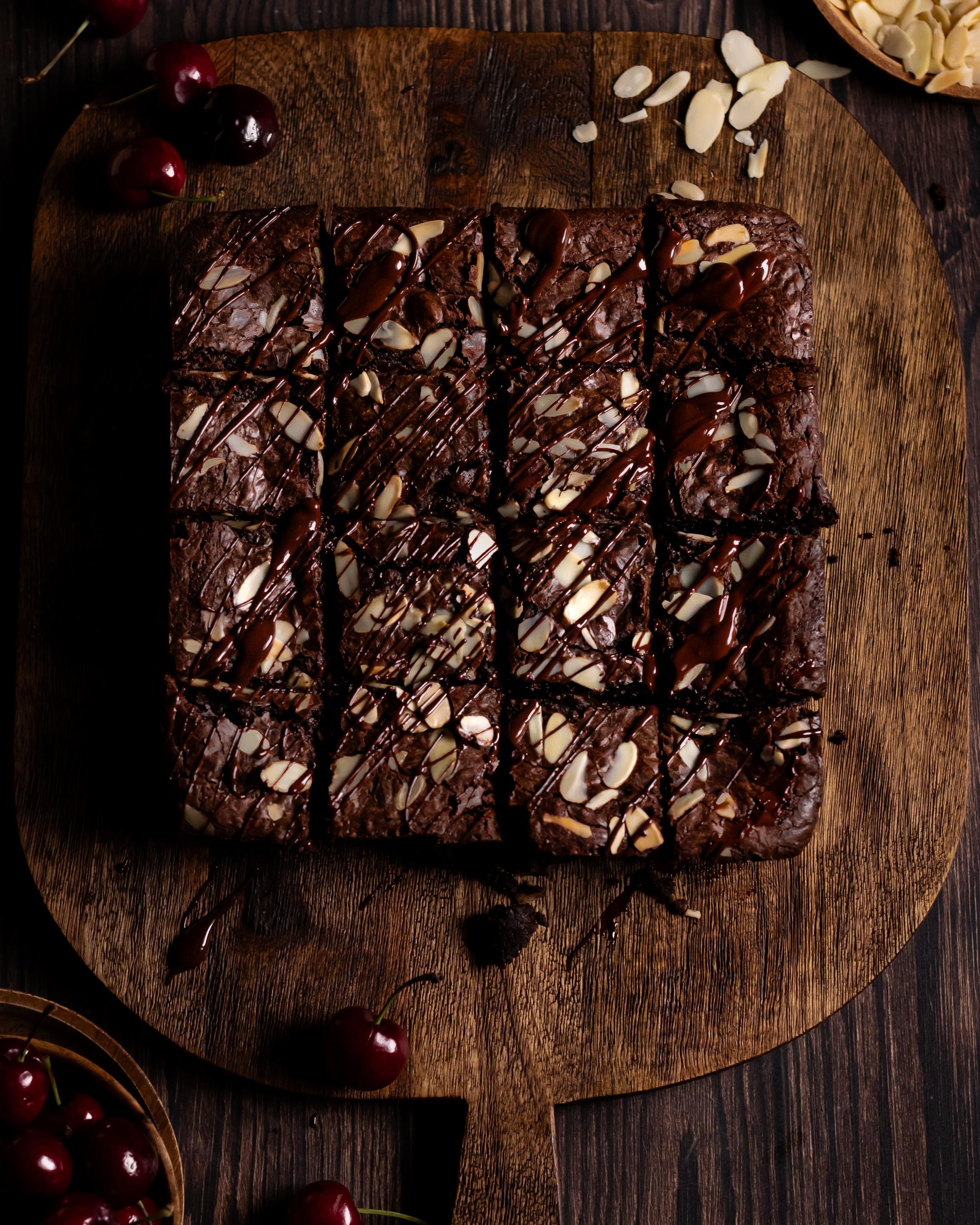a 16 piece batch of cherry and almond brownies, topped with melted dark chocolate and flaked almonds. Surrounded by fresh cherries and flaked almonds
