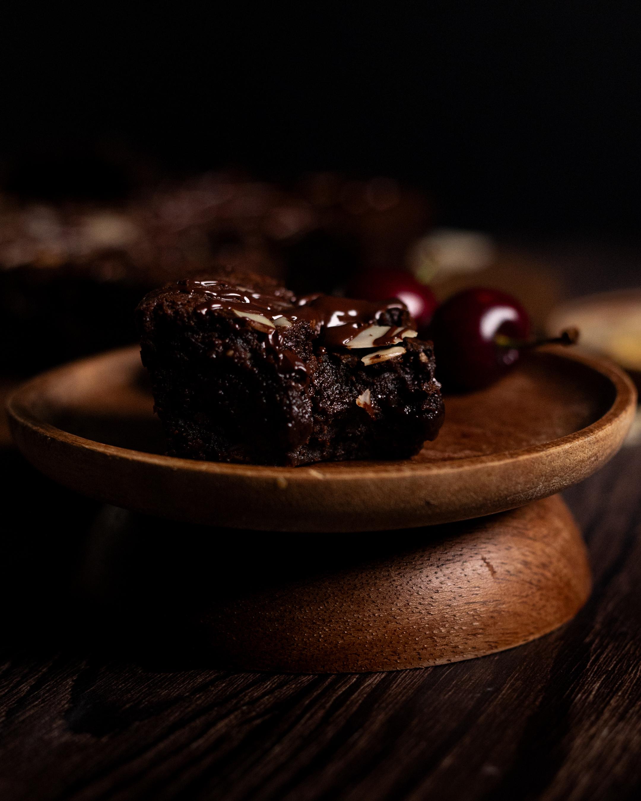 a single cherry and almond brownie with a bite taken out, surrounded by fresh cherries and brownies in the background 