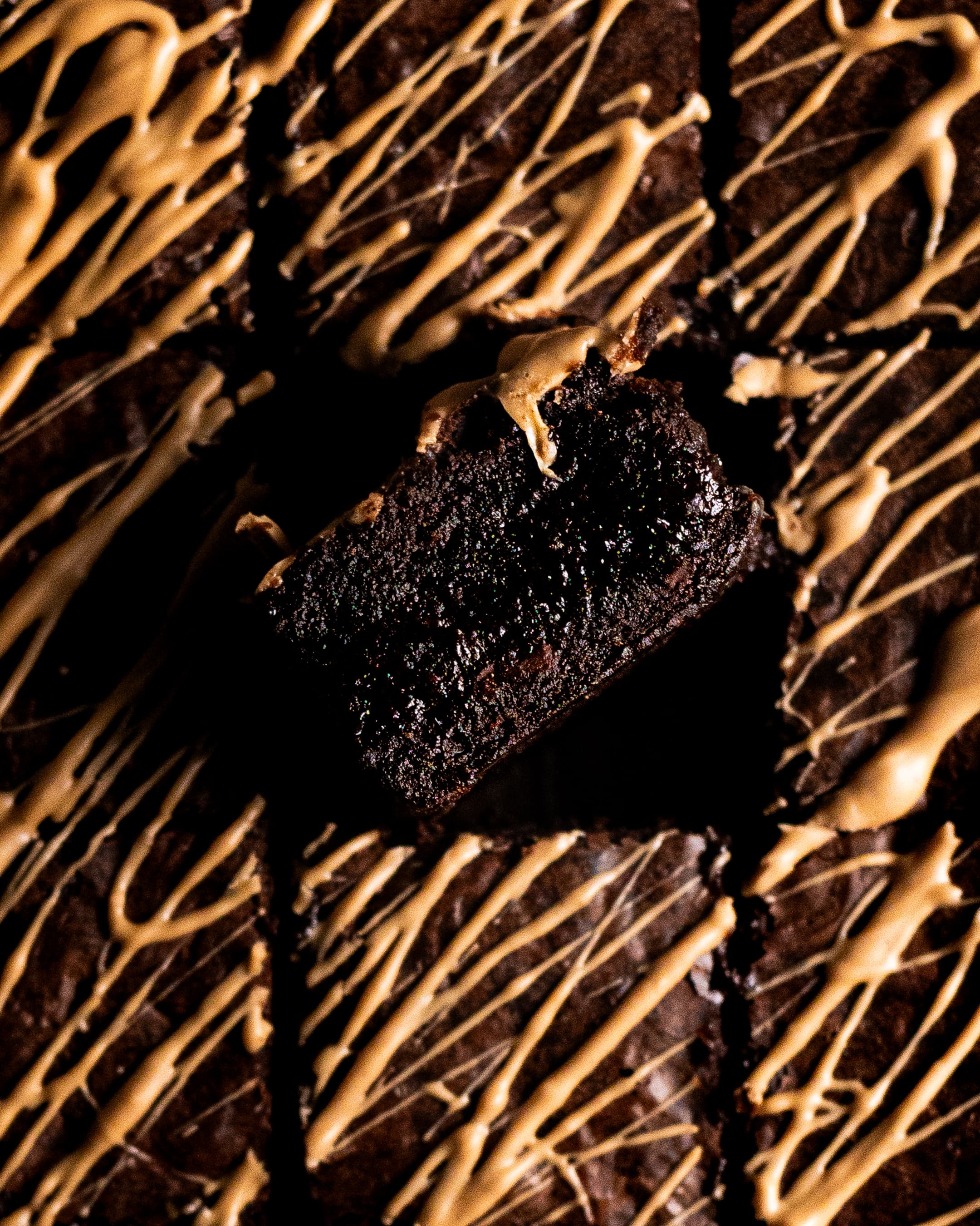 one chai brownie on its side showing its gooey centre, surrounded by chai brownies topped with gold chocolate 