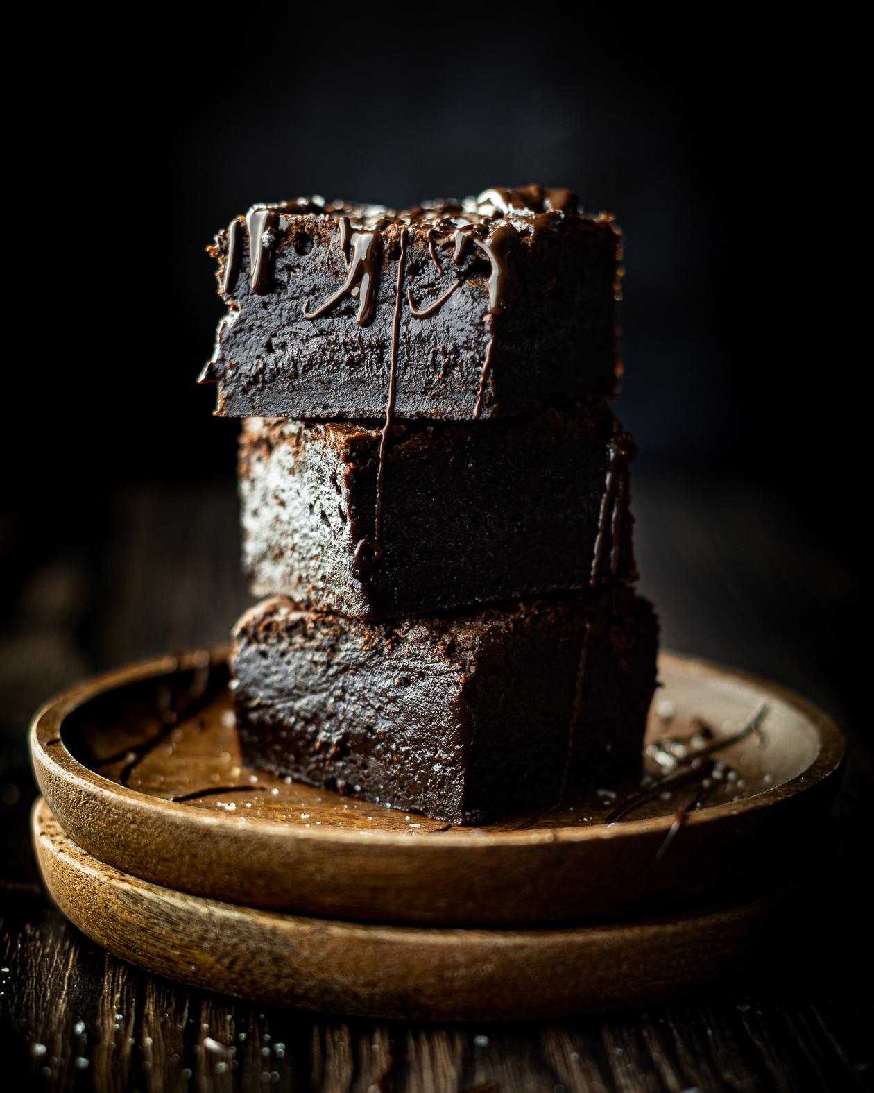 a stack of 3 dark chocolate brownies, topped with melted dark chocolate and sprinkled with sea salt 
