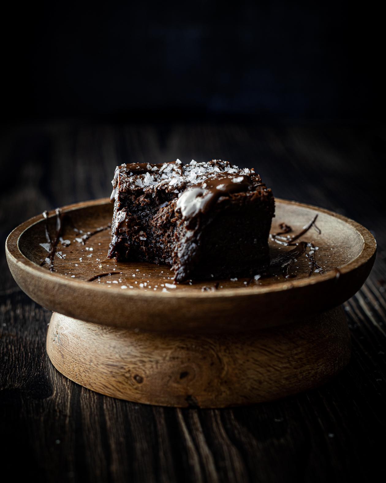 a single dark chocolate brownie with a bite taken out, topped with melted dark chocolate and sea salt