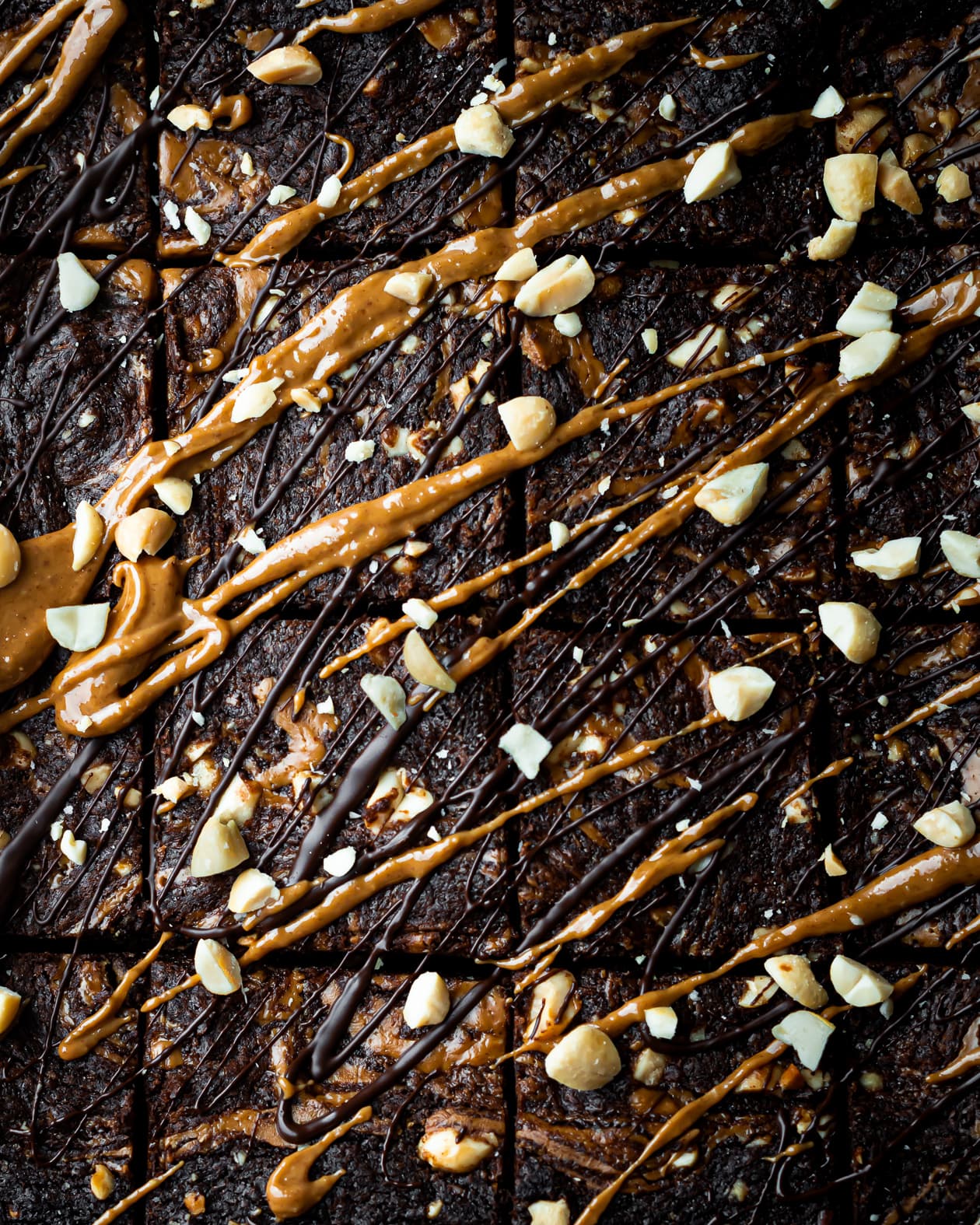 an overhead shot of 16 pieces of peanut butter and chocolate brownies. Topped with peanut butter, melted dark chocolate and crushed peanuts