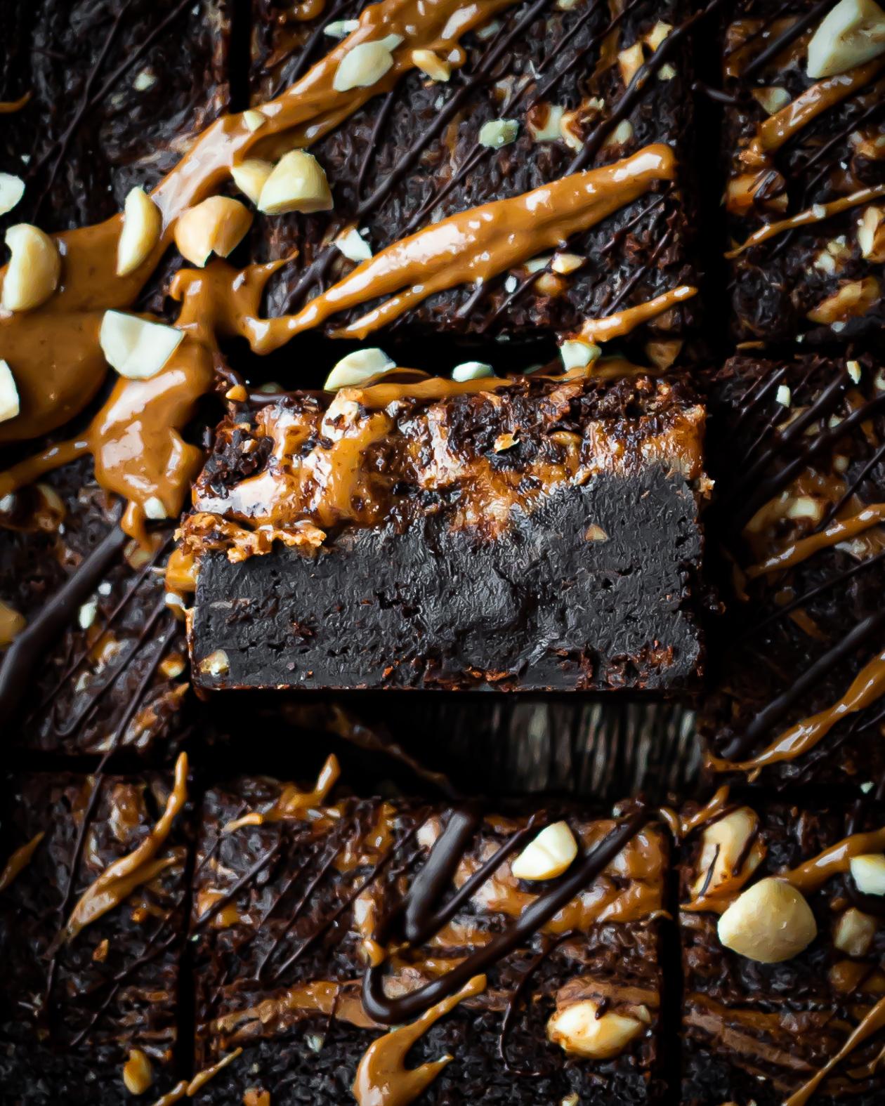 peanut butter and chocolate brownies, one brownie on its side showing thickness and density of brownies, topped with peanut butter, melted dark chocolate and crushed peanuts